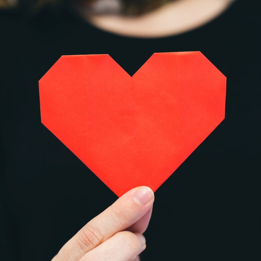 A person holding a red cutout heart with thumb and index finger