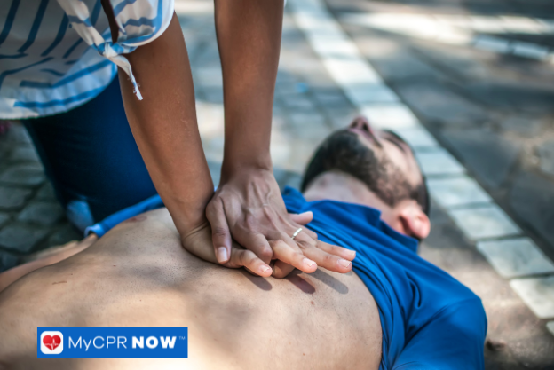A person performing CPR on a real individual lying on the ground, indicating an emergency resuscitation situation.