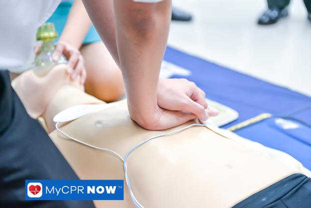 Hands performing chest compressions on a CPR mannequin during a training session.