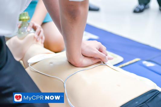 Hands performing chest compressions on a CPR mannequin during a training session.