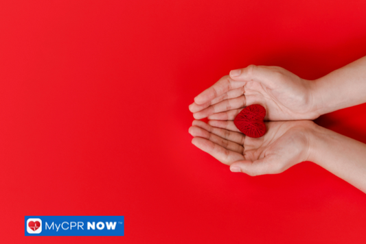 A pair of hands gently cradling a small red heart on a red background, symbolizing heart health and emergency care