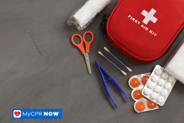 A first aid kit with scissors, tweezers, and medications on a gray surface.