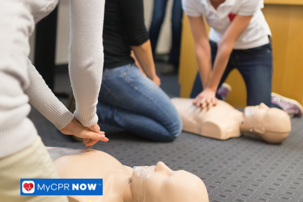 People practicing CPR on multiple training mannequins in a classroom setting.