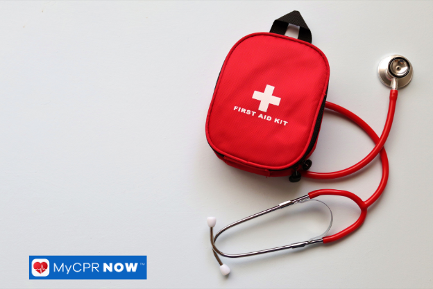 A red first aid kit next to a stethoscope on a light surface.