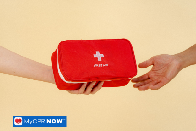 A red first aid kit being passed between two hands against a beige background.