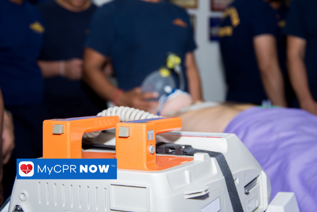 Defibrillator in the foreground with emergency responders providing CPR in the background.