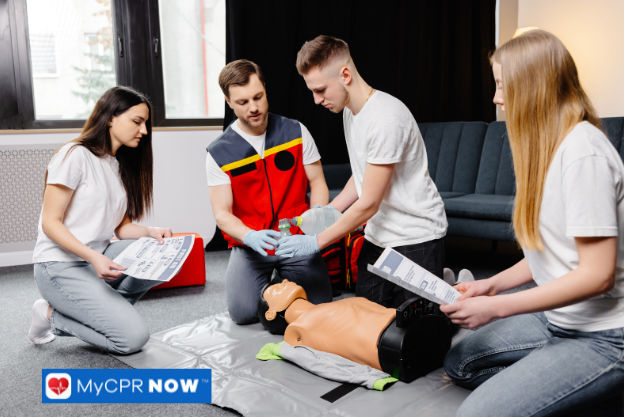 A group of people practicing CPR on a mannequin while receiving instruction indoors.