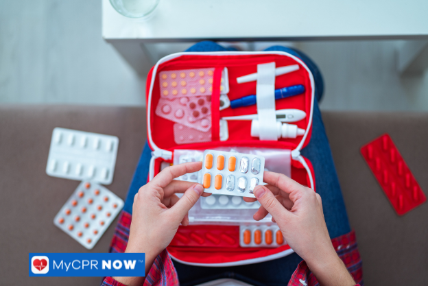 A person holding blister packs of medication with an open first aid kit on their lap.