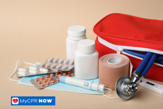 Open red first aid kit with bandages, pills, and a stethoscope on a beige surface.