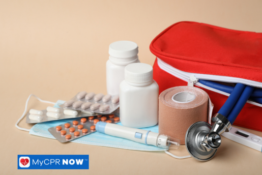 Open red first aid kit with bandages, pills, and a stethoscope on a beige surface.