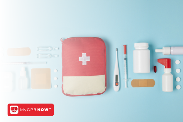 A red first aid kit with supplies like a thermometer, a needle, bottles, adhesive bandages, and pills on either side of it, all on a blue background. 