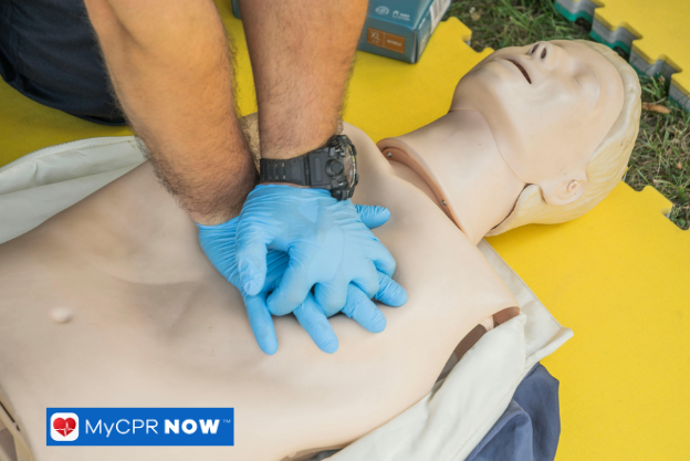 Hands performing chest compressions on a CPR training mannequin.