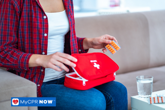 A person seated on a couch taking out medication from a red first aid kit.