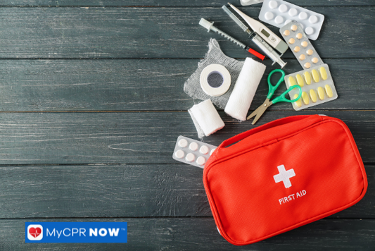 A red first aid kit with various medical supplies, including bandages, scissors, pills, and a thermometer, placed on a wooden surface.