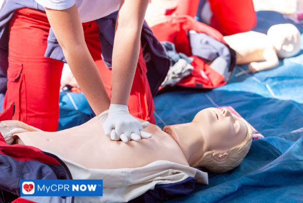 A CPR training session where a participant performs chest compressions on a manikin, supervised by an instructor in a red uniform.