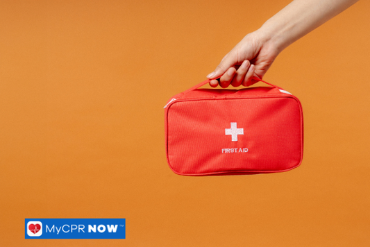 Hand holding a red first aid kit against orange background.