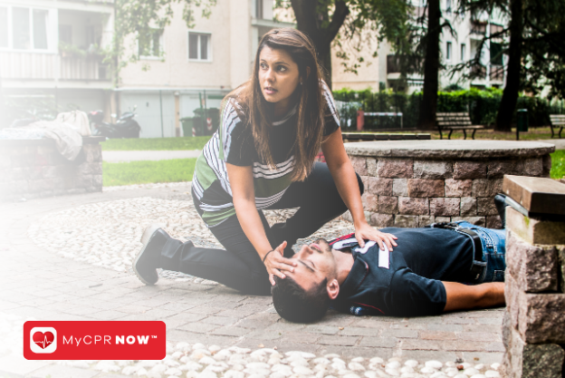 A first responder knelt down next to someone laying on the ground in a park. 