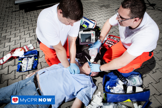 Paramedics in uniform attending to a person lying on the ground near an ambulance.