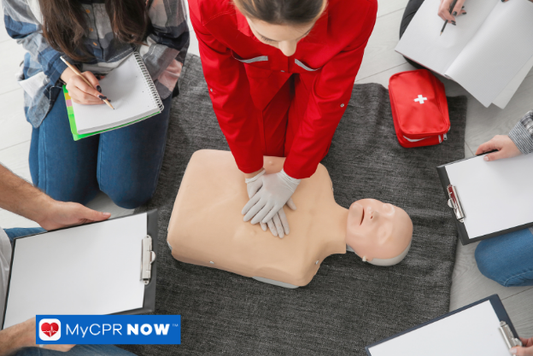 An instructor demonstrating CPR compressions on a manikin while others take notes.