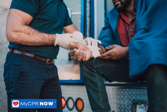 Medical worker bandaging a man’s hand near an ambulance.