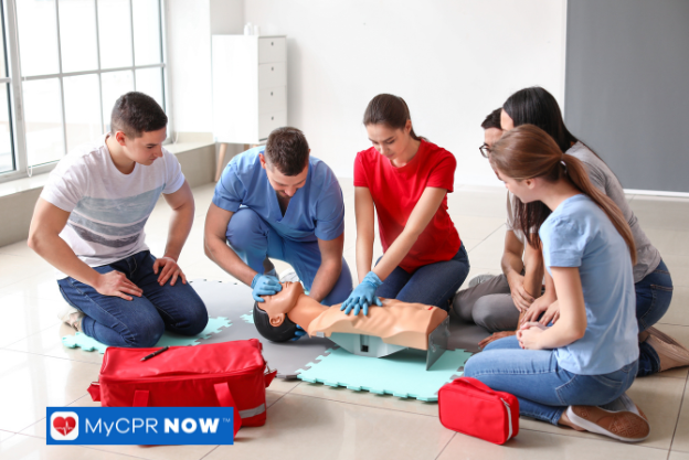 A CPR training session where a participant performs chest compressions on a manikin, supervised by an instructor in a red uniform.