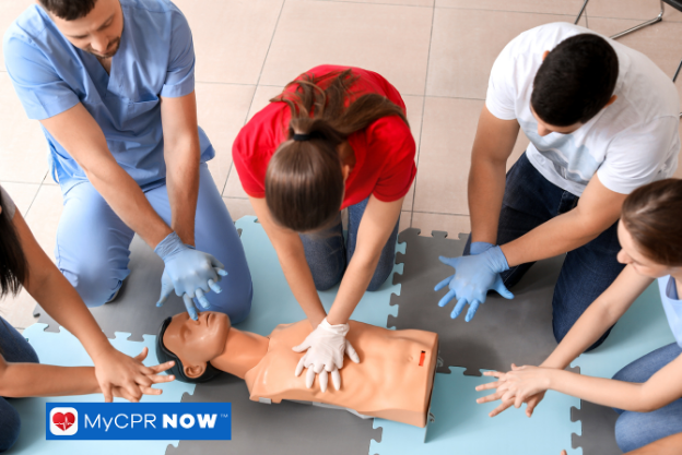 Several people gathered around practicing CPR compressions on a training mannequin.