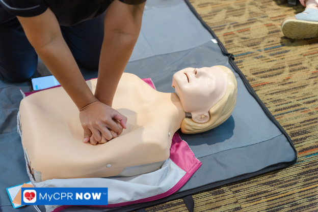 A person pressing down on a CPR mannequin's chest during a training session on a mat.