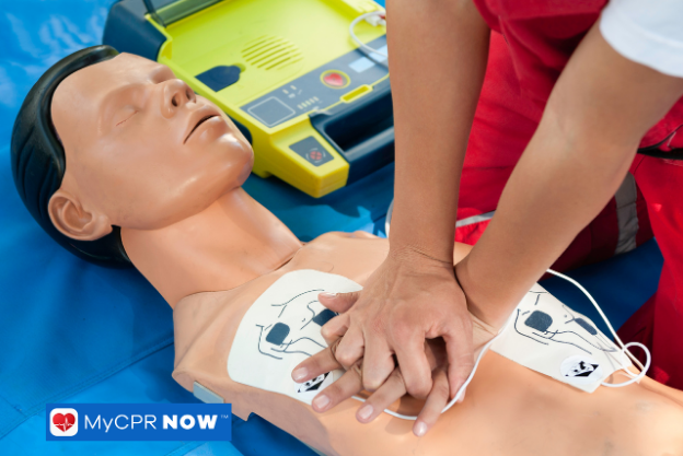 Person performing CPR on a training manikin with AED pads attached