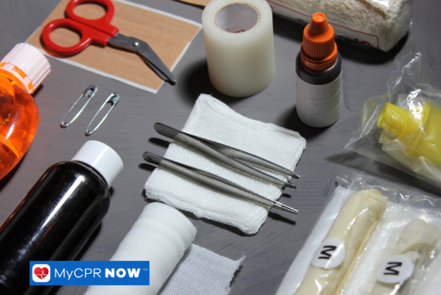 Assorted first aid supplies including bandages, tweezers, and tape on a dark background.