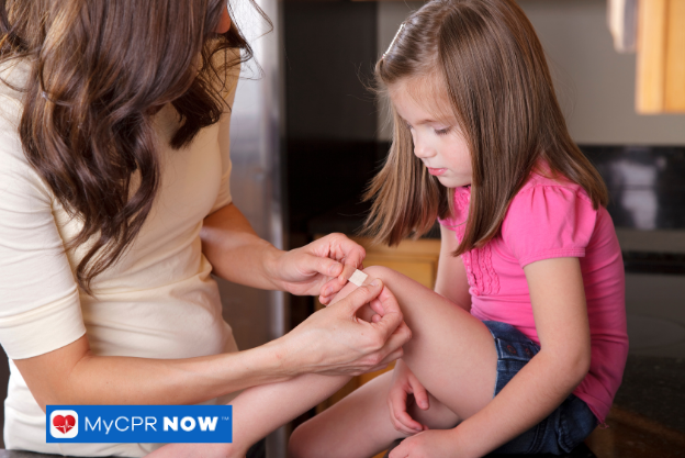 Woman applying a bandage to a young girl’s knee.