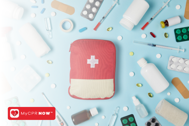 A red first aid kit on a blue background with first aid supplies all around it like syringes, pills, medical tape, bottles, and adhesive bandages. 