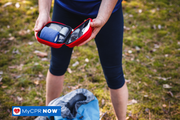 Person holding small red first aid kit outdoors.