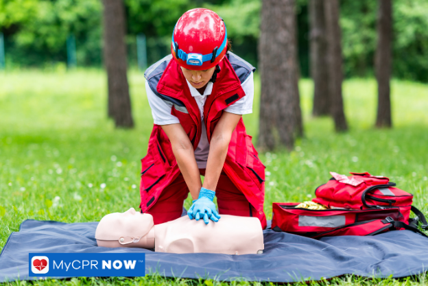 Rescue worker performing CPR compressions on a manikin in a forest training scenario.