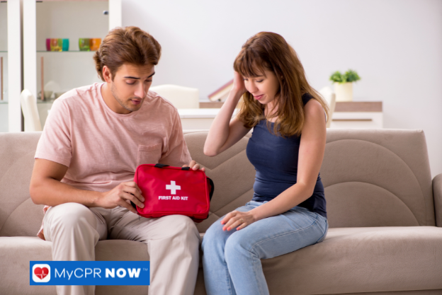 A man and woman sitting on a couch, with the man holding a red first aid kit.
