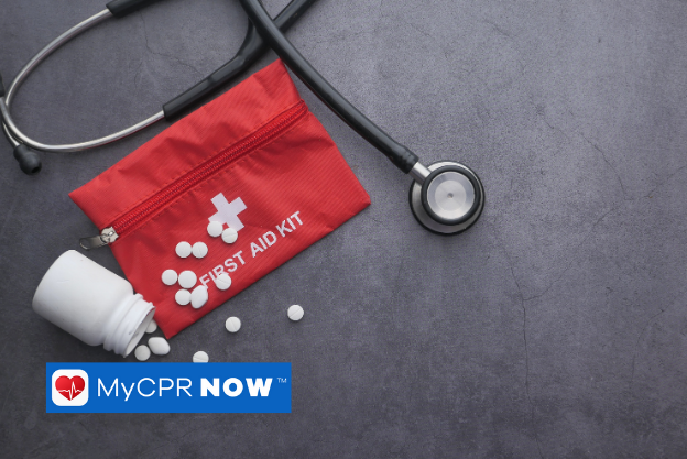 A red first aid kit with a stethoscope and pills on it with a dark grey background.