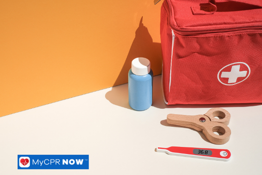 First aid kit with supplies – A red first aid bag with scissors, a thermometer, and a small bottle against an orange wall.