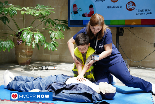 Child learning CPR with instructor – A child practices chest compressions on a CPR manikin under the guidance of an instructor.
