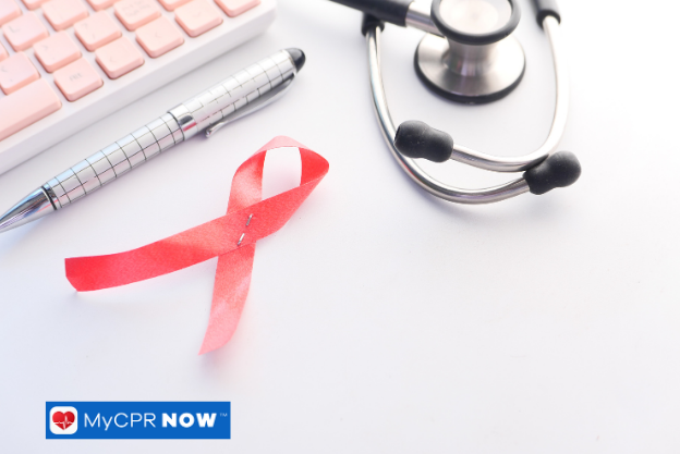 Red ribbon awareness symbol with stethoscope and keyboard on a white surface.