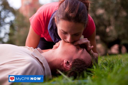 Woman performing rescue breaths on a man during CPR outdoors.