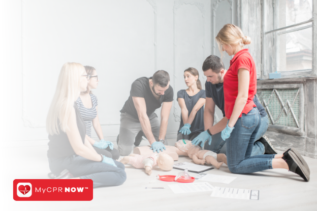 A group of people inside around two infant CPR mannequins practicing CPR chest compressions. 