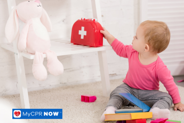 Baby reaching for a red first aid kit on a white shelf with toys around