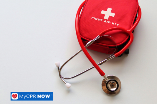 A red first aid kit with a white cross and a stethoscope placed on a white surface.