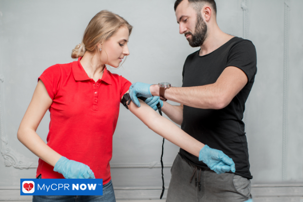 Applying a tourniquet on a person’s arm during a first aid demonstration.