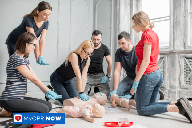 Group practicing CPR on training manikins in a classroom setting.
