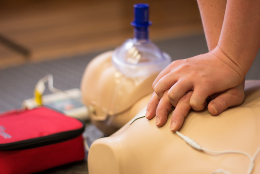 A close up of someone's hands practicing CPR chest compressions on an adult CPR mannequin.  