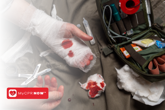 Someone with a bandaged hand that has some blood on it with a open first aid kit next to them. 