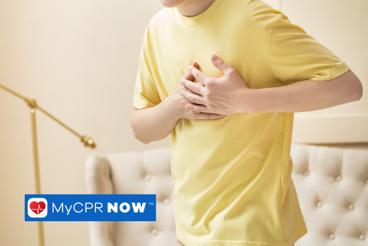 Someone in a yellow shirt holding their chest with a white couch behind them. 