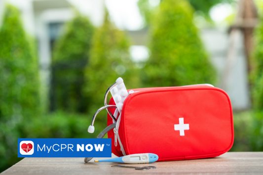 A red first aid kit with pills and a stethoscope coming out of it and a thermometer infront of it on a table outside. 