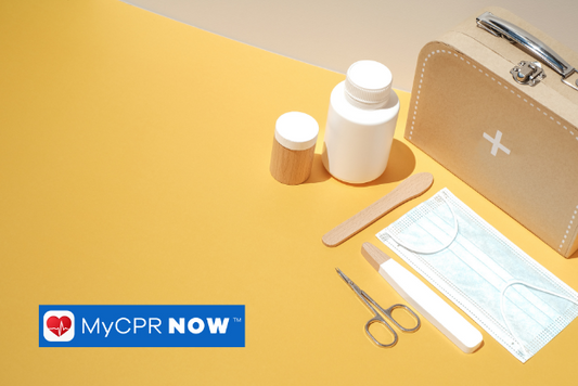 A tan first aid kit with bottles, a mask, tongue depressor, and scissors in front of it on a yellow surfance.