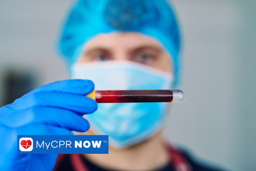 A medical professional wearing PPE holding a vile of blood. 